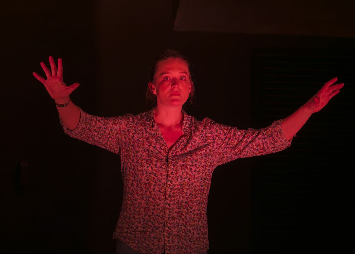 Sybille Montagne, bras grands ouverts sous une lumière rouge